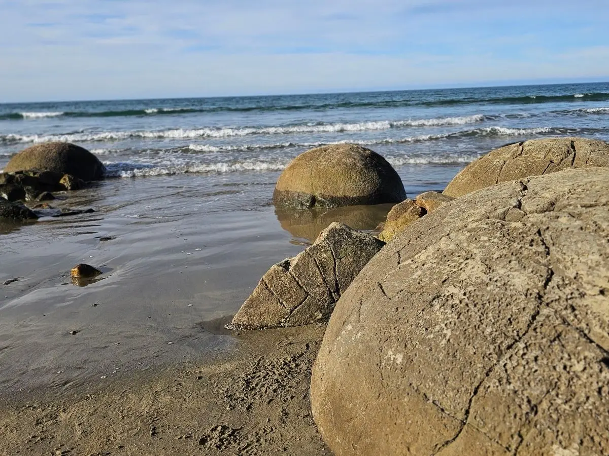 Moeraki Boulders on Koekohe Beach, showing cracked surfaces and wet sand at low tide